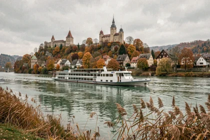 Bateau de croisière sur le Rhin longeant un village médiéval allemand avec châteaux sur les collines en automne
